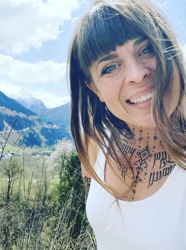 Yogalehreren Fia Sonora ist im Freien und lächelt während man im Hintergrund das Bergpanorama sieht.